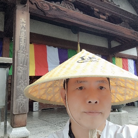 菅笠をかぶり、寺院の前に立つ平貞さん