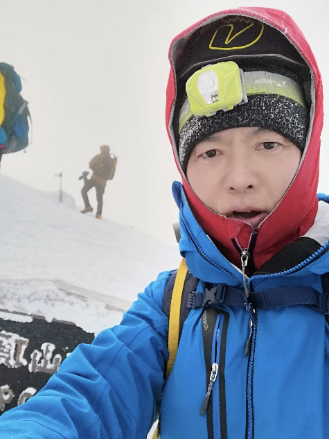 雪山で青いジャケットとヘッドライト付きの帽子を身につけた平貞さん